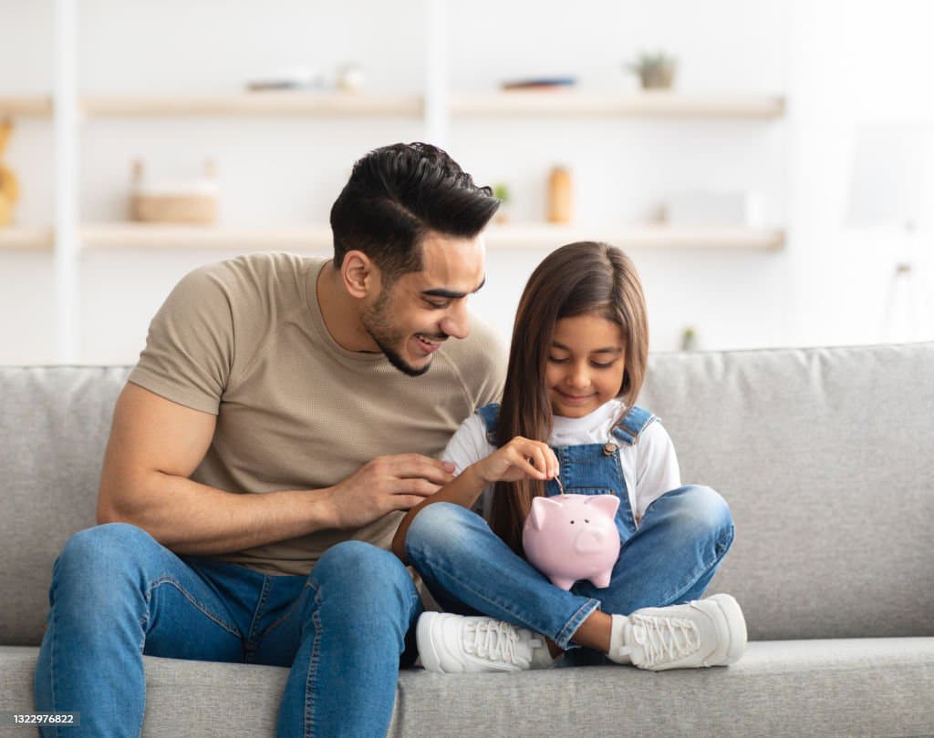 Father and daughter with piggy bank on a couch